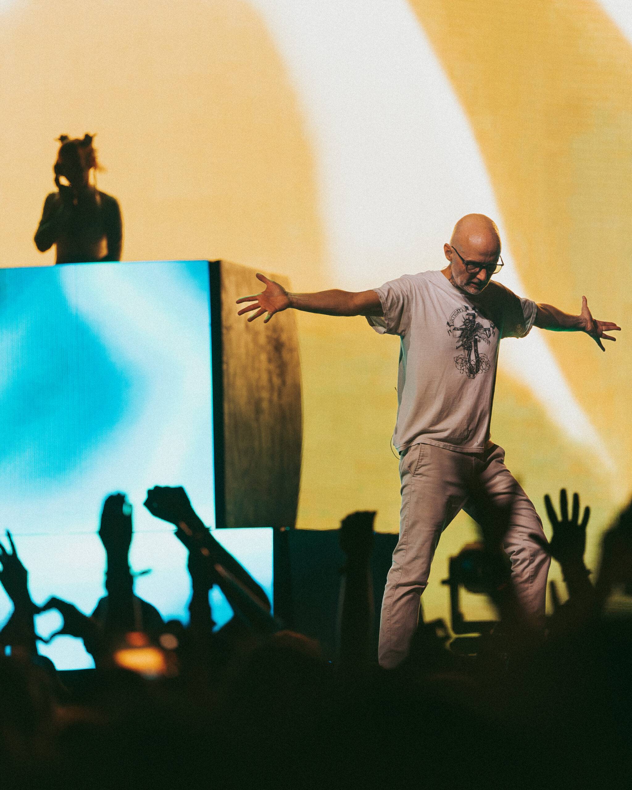 Picture of Moby performing at Coachella 2026. He is standing on the stage while the silhouettes of cheering audience members rise up from below