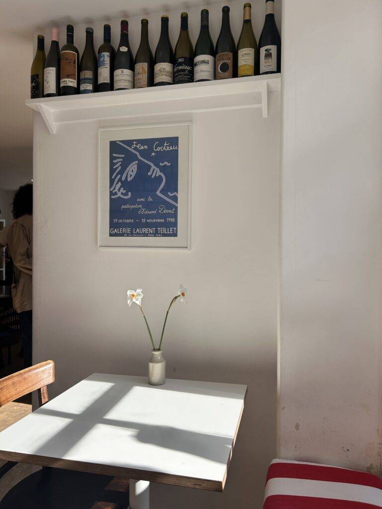 A picture of sunshine through onto an empty table with some wine bottles on a shelf in the background