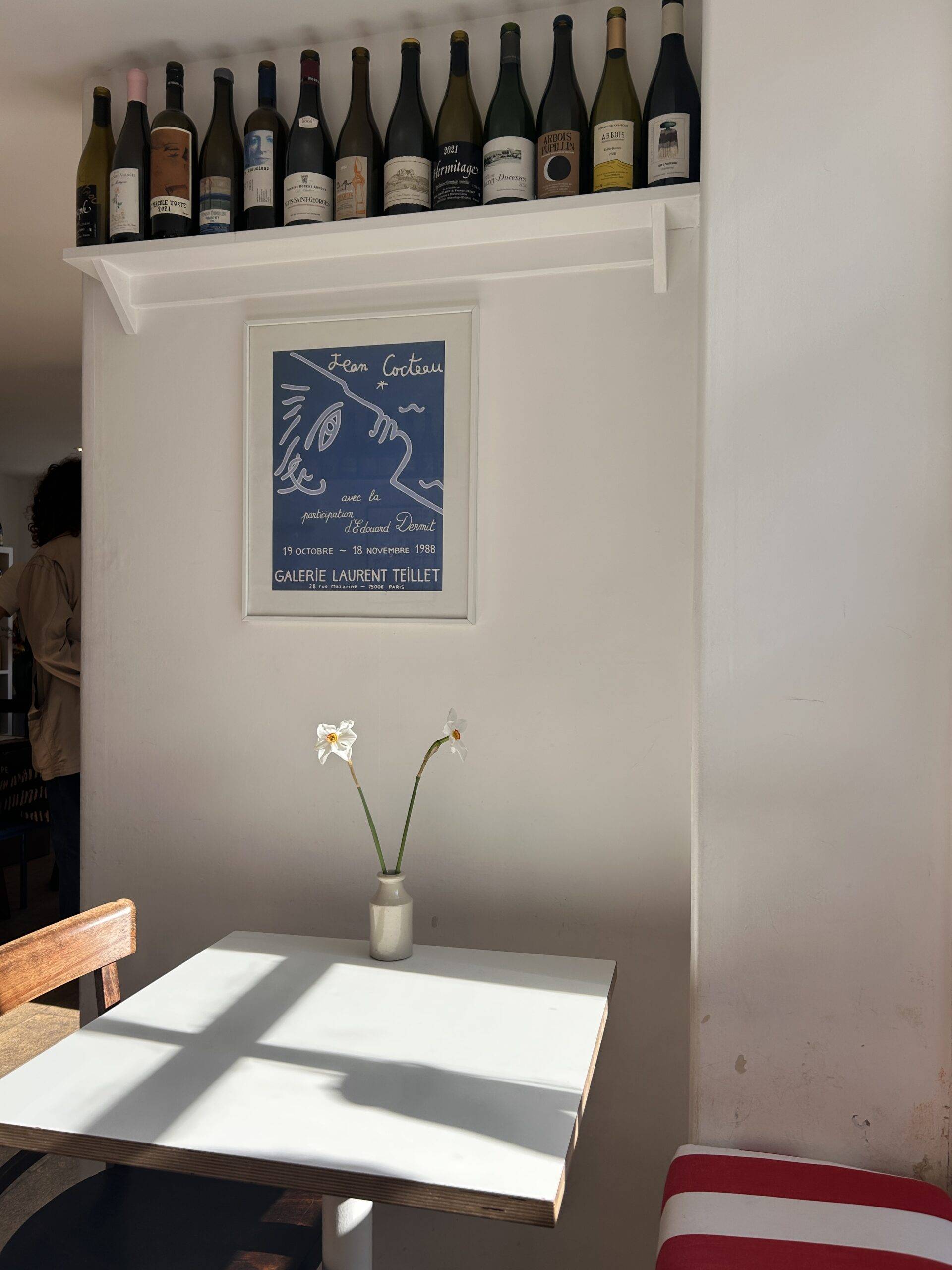 A picture of sunshine through onto an empty table with some wine bottles on a shelf in the background